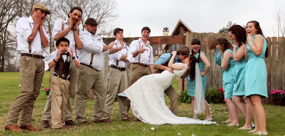 Posed bridal party shot with newlyweds kissing