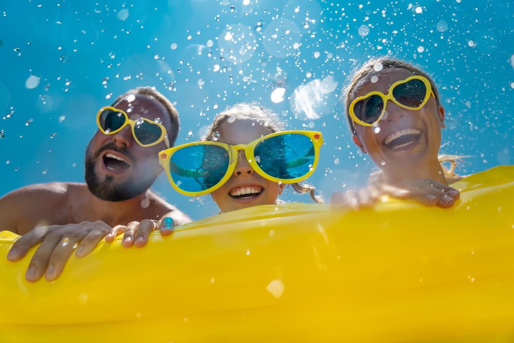 A family of three, smiling, rides a waterpark tube during their summer getaway in East Texas.